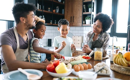 An Afro-latino family laughs while making food together in their kitchen