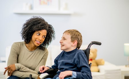 Female caretaker sitting next to a boy with disabilities in a wheelchair