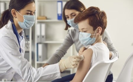 Doctor in medical face mask giving vaccine injection to young child