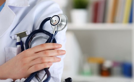 Close-up of the left shoulder of a doctor in a white lab coat, their right hand is visible, holding their stethoscope