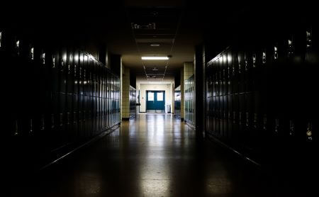 Straight view of darkly lit hallway with bright light at end and lockers covering the walls on either side