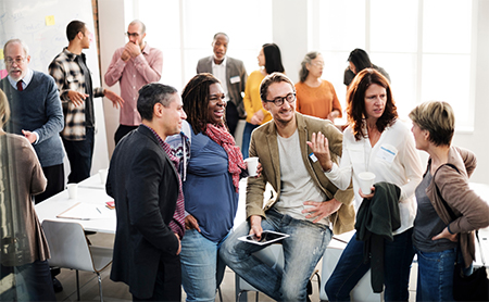 A diverse group of meeting attendees talk casually in clusters