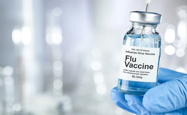 Hand of a gloved medical professional holding a flu vaccine ampoule, syringe is removing some of the vaccine