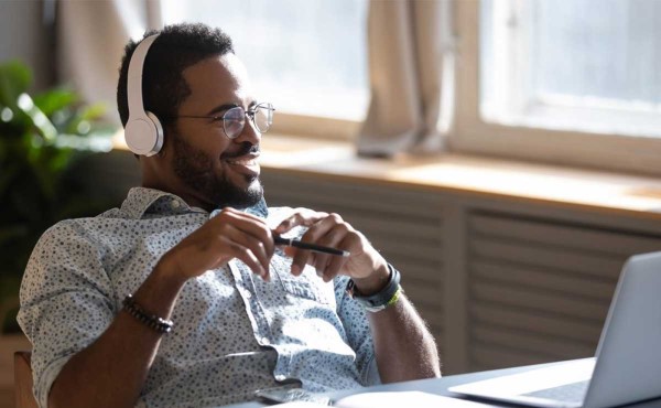 Man sitting at his desk, smiling, listening to headphones