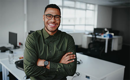 A Black man in his office smiles broadly at the camera