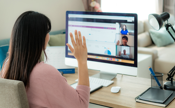 A woman sitting at her desk, on a teleconference, greeting coworkers